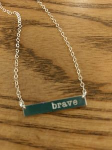 A simple silver necklace with the word "brave" engraved on a silver bar..