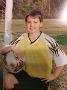 Jayden's soccer picture. He's kneeling on one knee and holding the soccer ball.